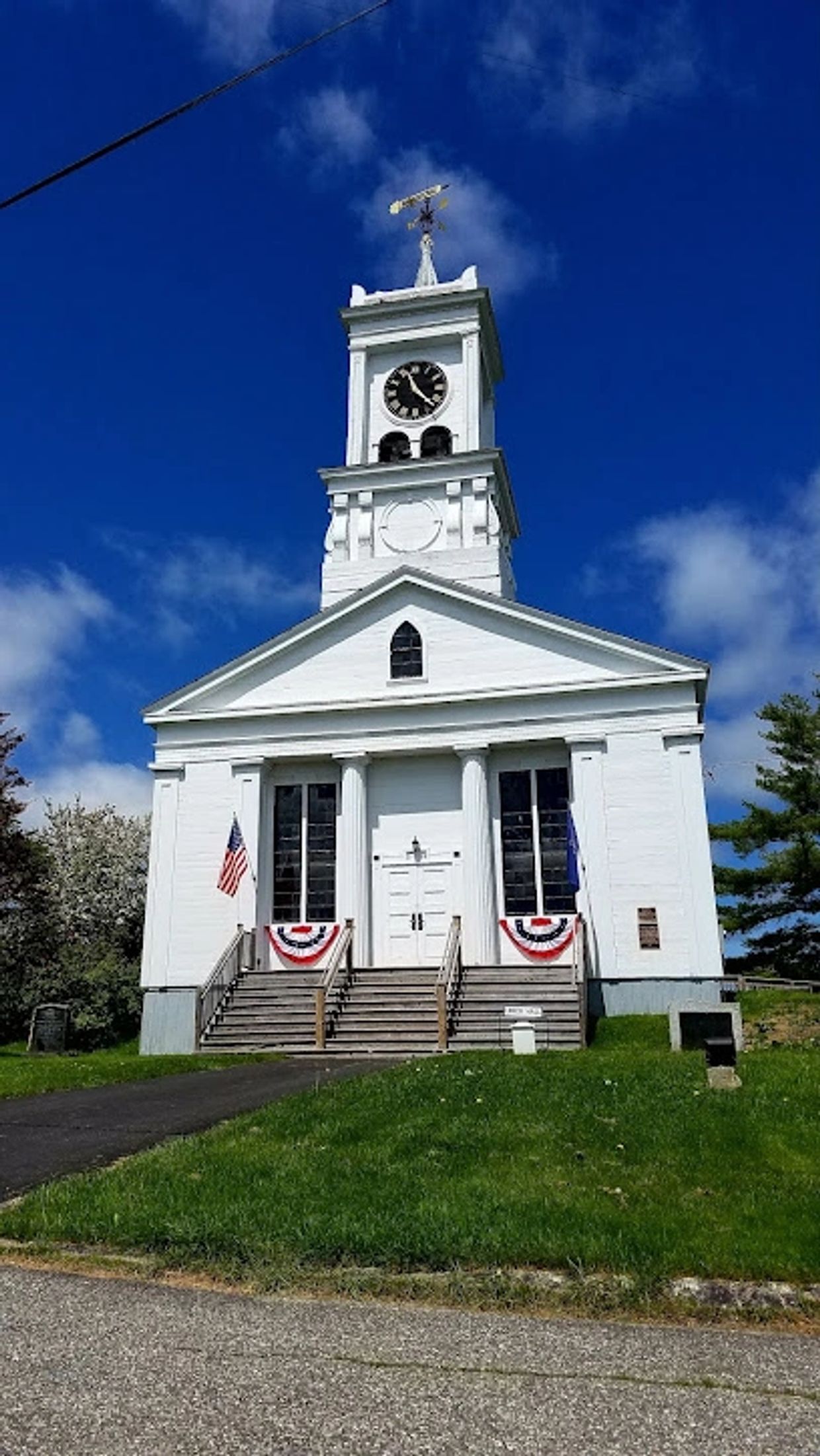 White church with clock tower under blue sky and American flags.
