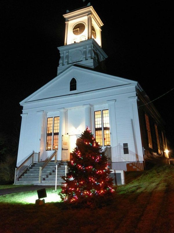 A white church at night with a lit Christmas tree in front.
