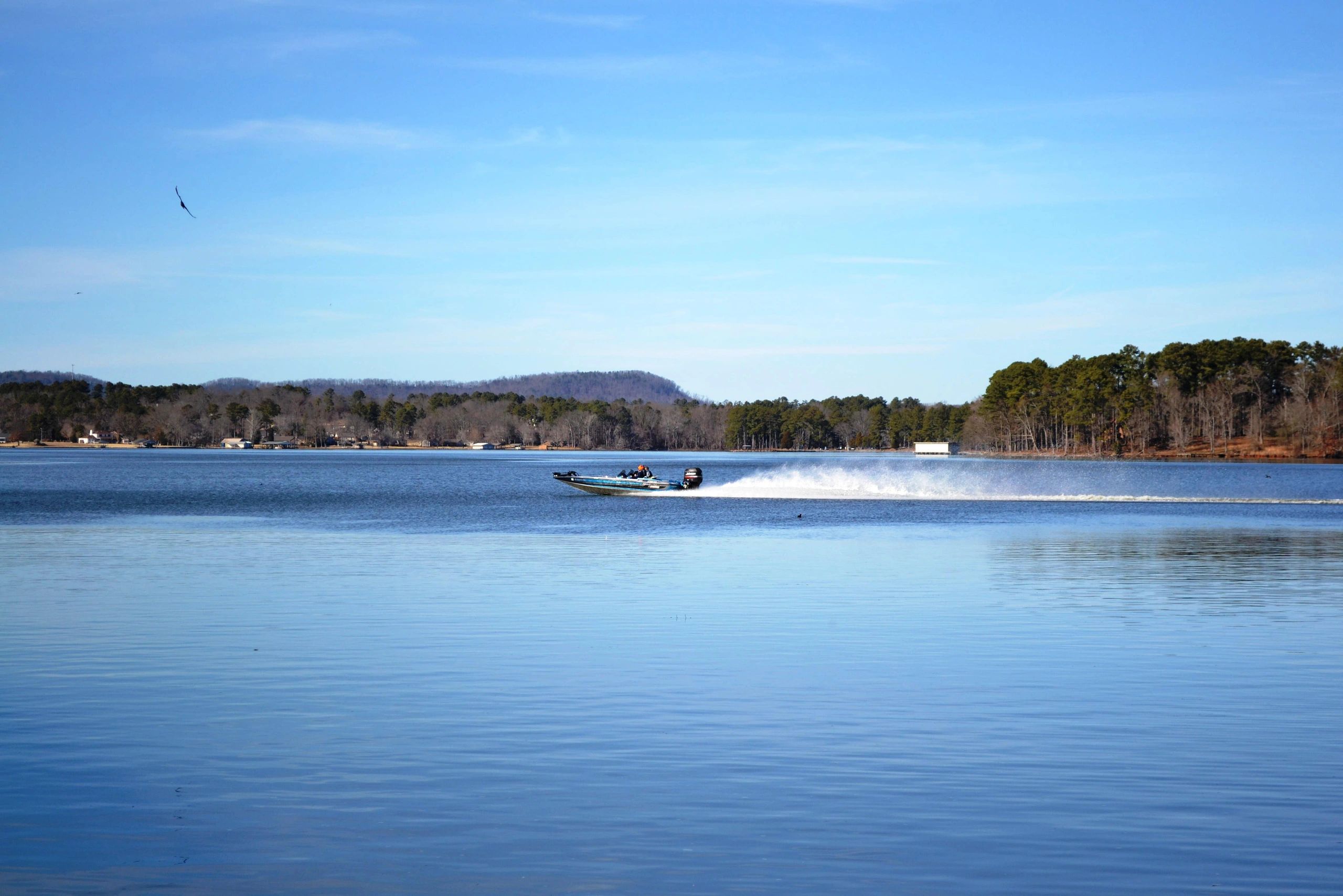 A speedboat races across a calm lake under a clear blue sky.