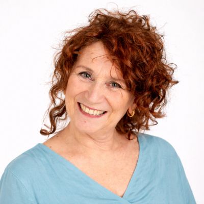 Smiling woman with curly red hair wearing a light blue top.