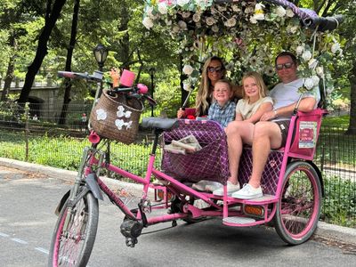 Family riding a decorated pink pedicab in a park.
