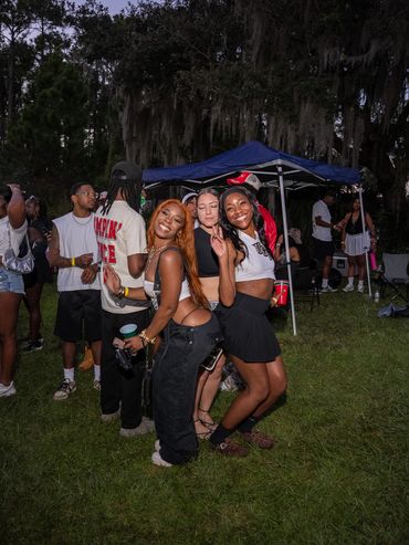 Three friends smiling and posing at an outdoor party with a tent in the background.