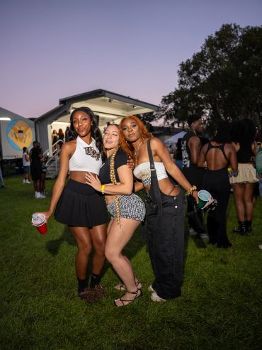 Three friends posing together at an outdoor event during twilight.