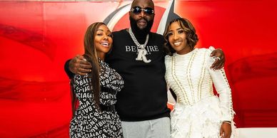 Three people posing together in front of a red background.