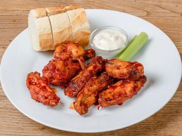 7 Chicken Wings in einer scharfen Soße mit einem Dip, Brot, Sellerie auf einem Teller