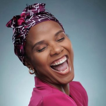 Joyful woman laughing with eyes closed, wearing a patterned headscarf and pink outfit.