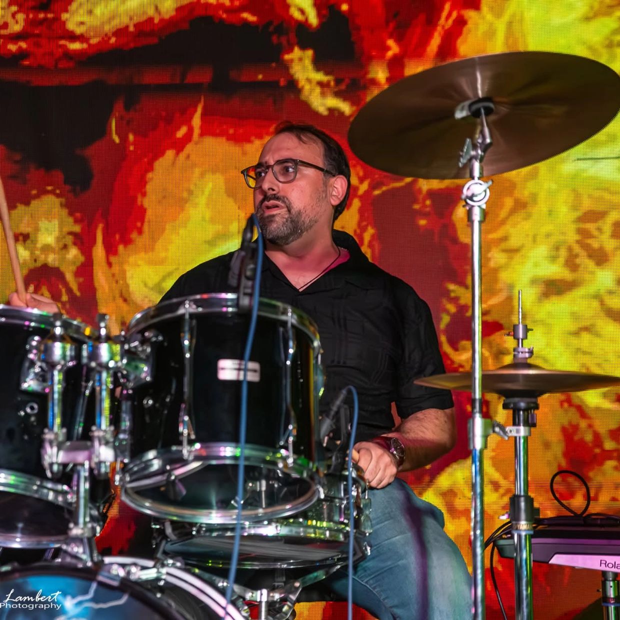 Man playing drums with fiery background on stage.