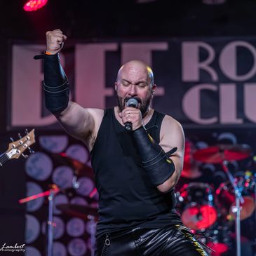 Energetic male rock singer in black leather performs passionately on stage.