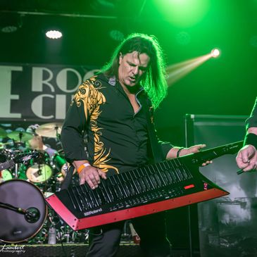 Musician passionately playing a keytar on stage under green lighting.