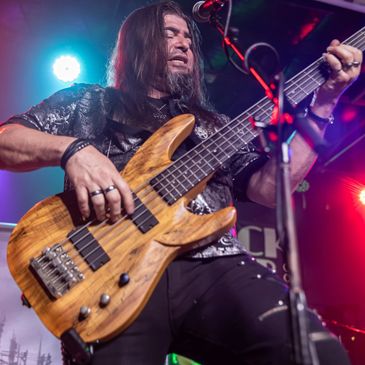 Musician passionately playing a wooden electric bass guitar on stage with colorful lights.