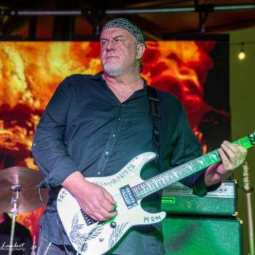 Man playing an electric guitar on stage with intense expression.