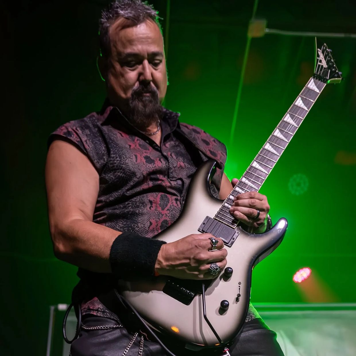 Musician passionately playing electric guitar on stage with green lighting.