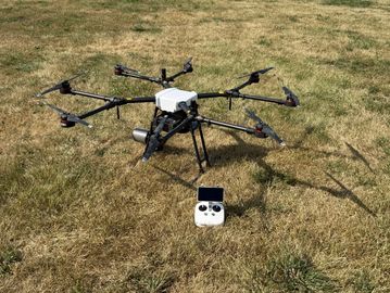 A large octocopter drone with a remote controller on dry grass.