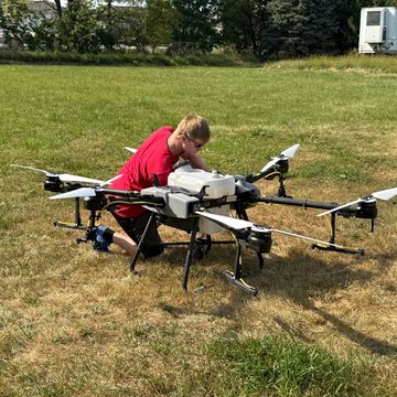 Person kneeling on grass, working on a large drone with multiple propellers.