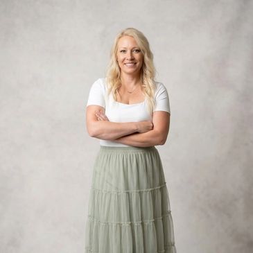 Smiling woman in white top and green skirt with arms crossed.
