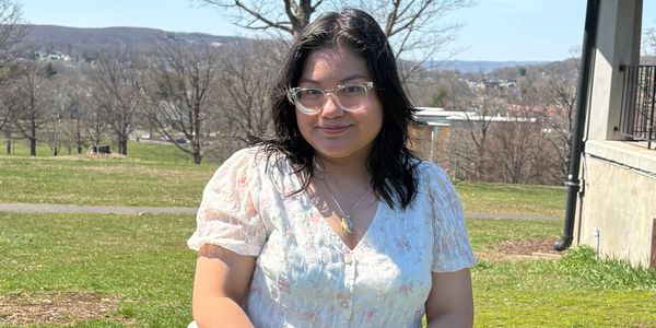 Young woman with glasses sitting on grass outdoors on a sunny day.