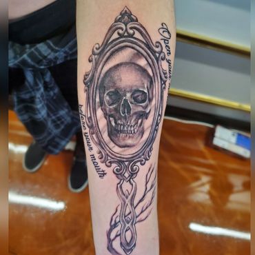 black and greay realism on forearm. Realistic skull inside a victorian gothic mirror. Macabre tattoo