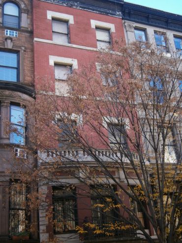Old brick building with boarded windows and a leafless tree in front.