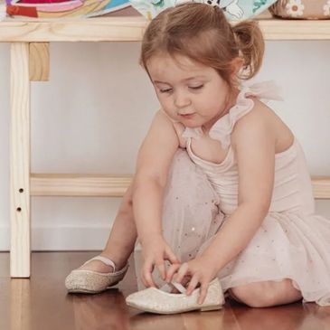 Little dancer crouched down putting her shoes on.