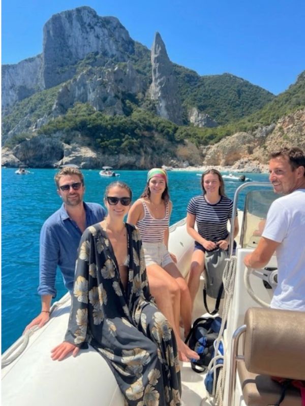 Five friends enjoying a sunny boat ride near rocky cliffs and clear blue water.