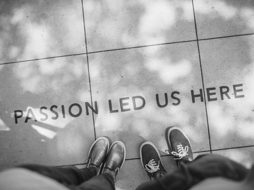 Two people standing near text on the ground that reads 'PASSION LED US HERE'.