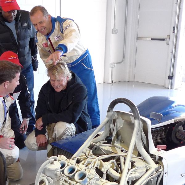 Group of guys laughing at a race car that had caught on fire