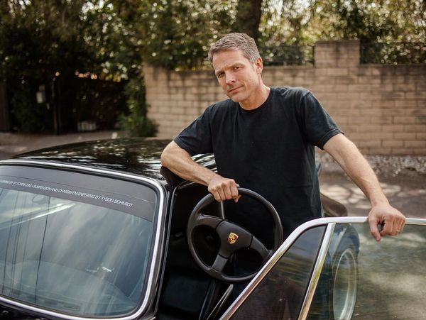 A hansom man standing next to a Porsche