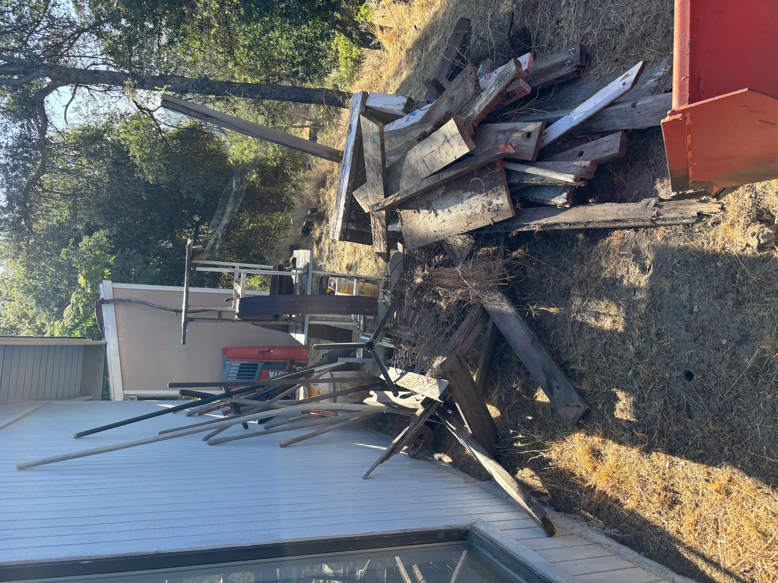 Outdoor area cluttered with wooden planks, tools, and metal objects near a white building.