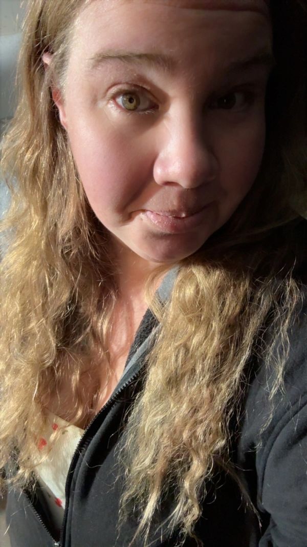 Woman with blonde curly hair and green eyes in soft natural light.