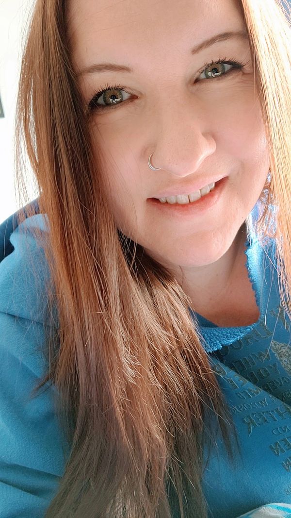 Close-up of a smiling woman with long hair and a nose ring.
