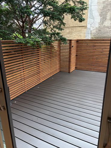 Empty outdoor wooden deck with horizontal wooden fence and tree.
