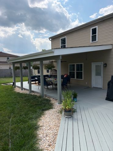 Covered outdoor patio attached to a house with seating and greenery.