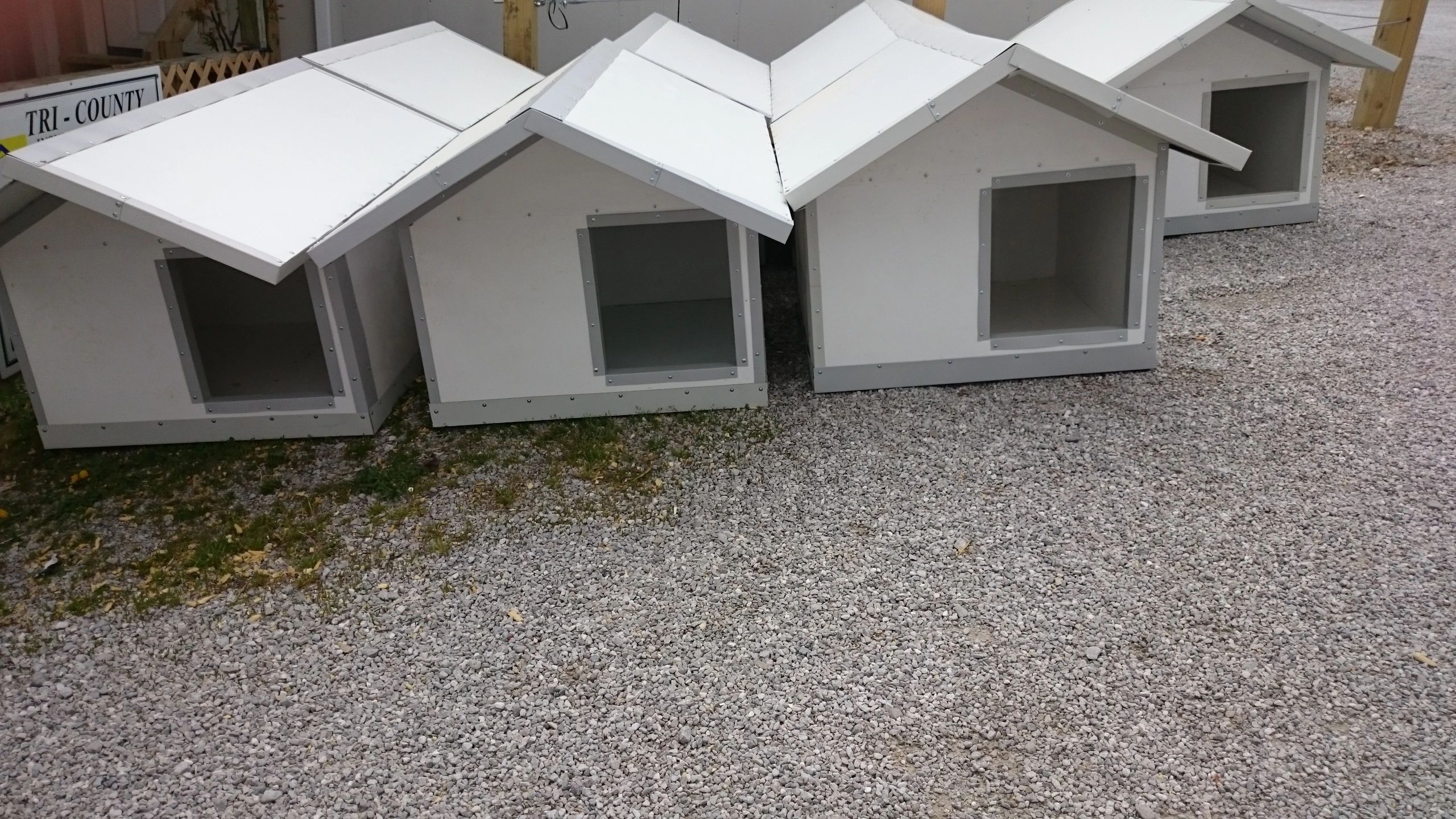Four white dog houses lined up outdoors.