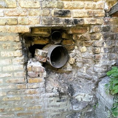 Old brick wall with a damaged pipe protruding.