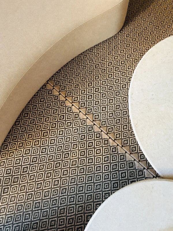 Patterned carpet meeting beige curved sofa and white round tables.