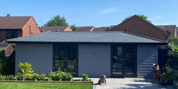 Modern backyard garden room with gray cladding and large windows.