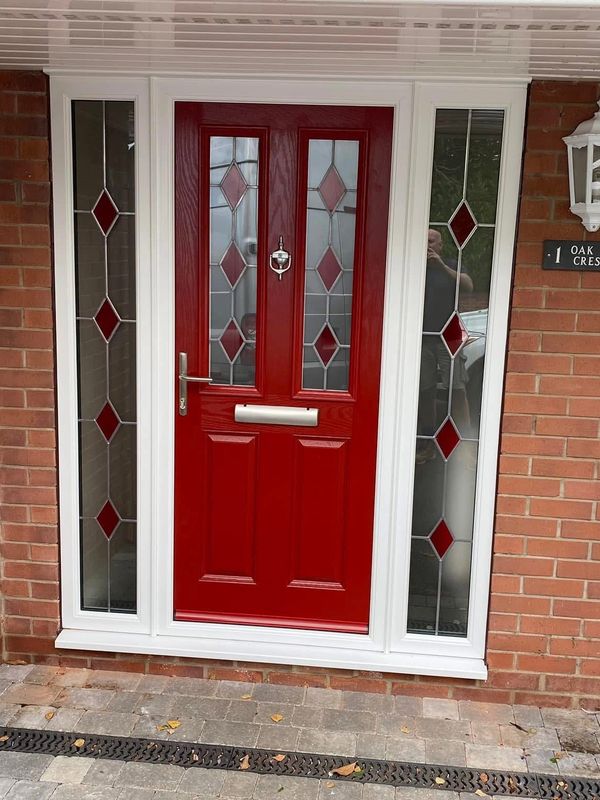 Red front door with decorative glass panels and white frame on brick house.