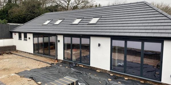 Modern single-story house with large glass doors and skylights under construction.