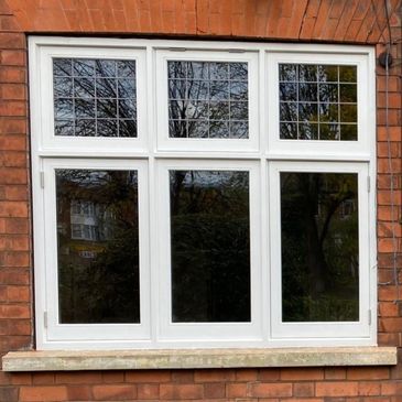 White framed window on a red brick wall reflecting trees.