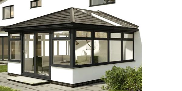 Modern sunroom with large windows and dark frame attached to a white house.
