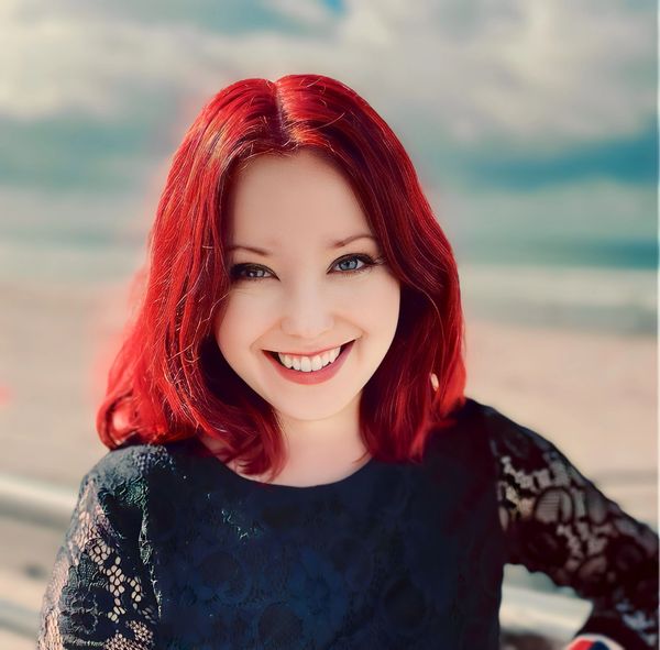 Smiling woman with vibrant red hair and blue eyes wearing a black lace top.