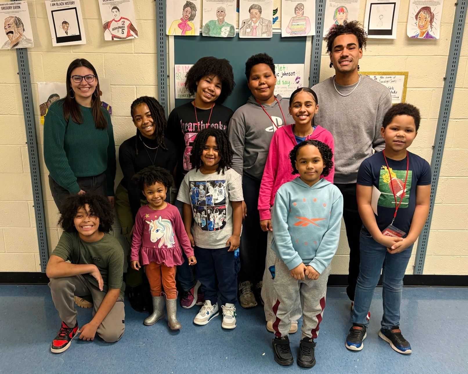A diverse group of children and two adults smiling in a classroom.
