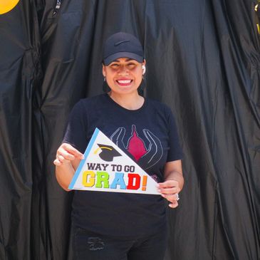 Smiling graduate holding a colorful 'Way to Go Grad!' sign.