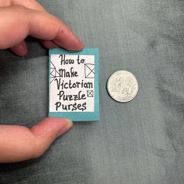 Miniature book titled 'How to Make Victorian Puzzle Purses' next to a quarter.