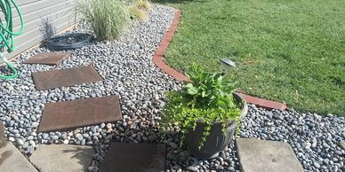 A garden path with stepping stones and a potted plant on gravel beside a lawn.