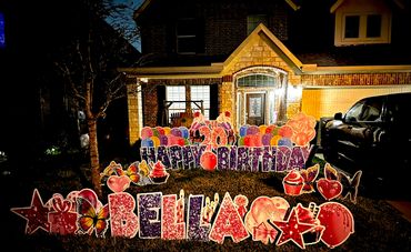 Colorful birthday decorations with 'Bella' displayed on a lawn at night.