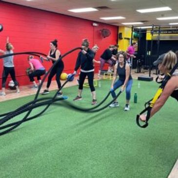 People exercising with battle ropes and medicine balls in a gym.