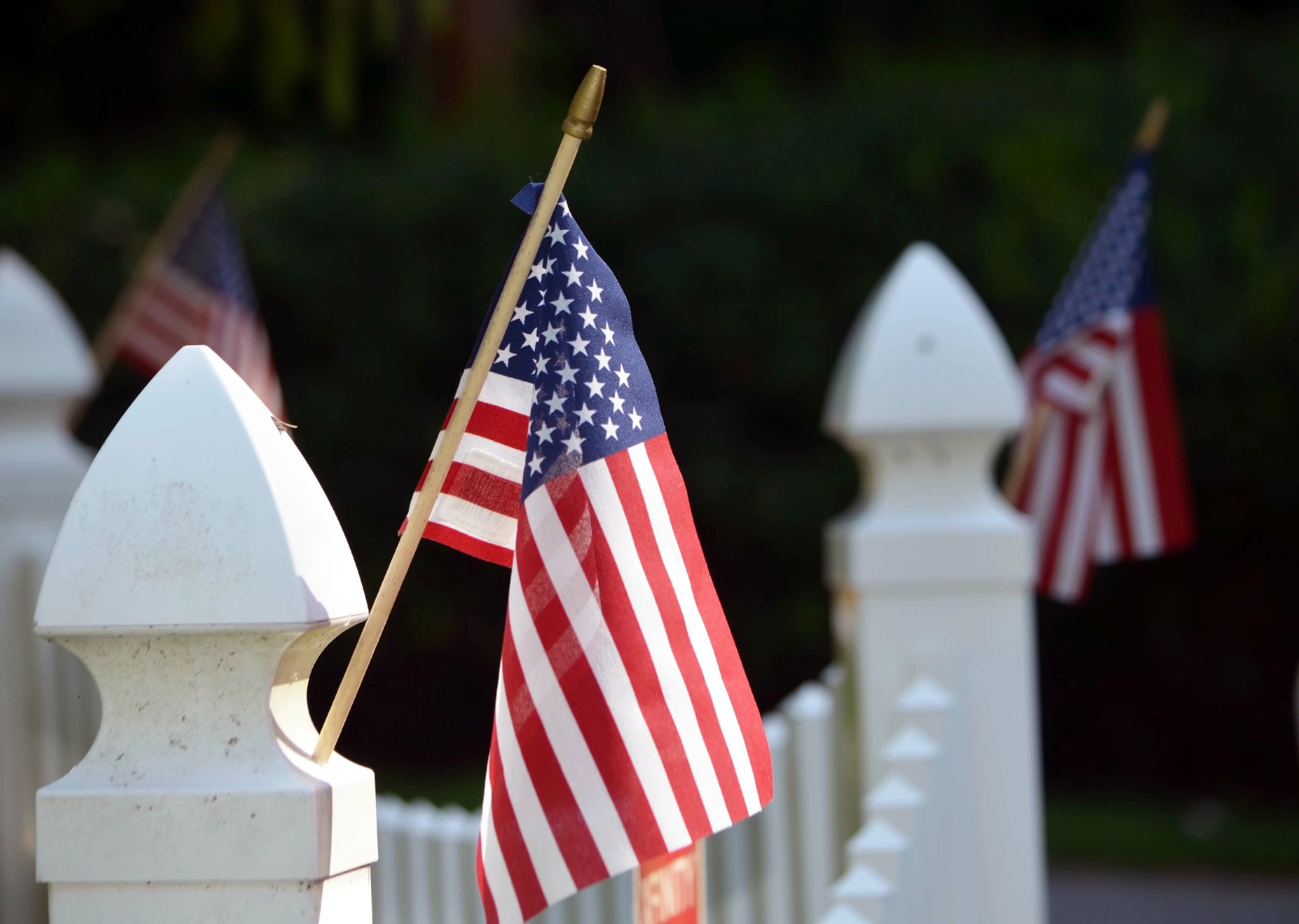 Up close picture of a white fence post with an American flag attached.