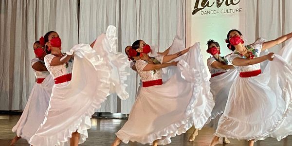 Dancers in white dresses and red masks performing a cultural dance.