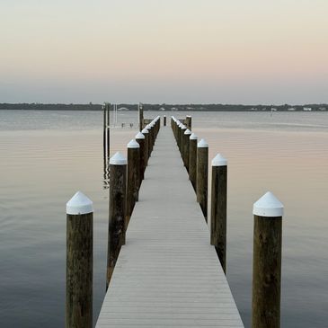 A long wooden dock extending into calm water at sunset.